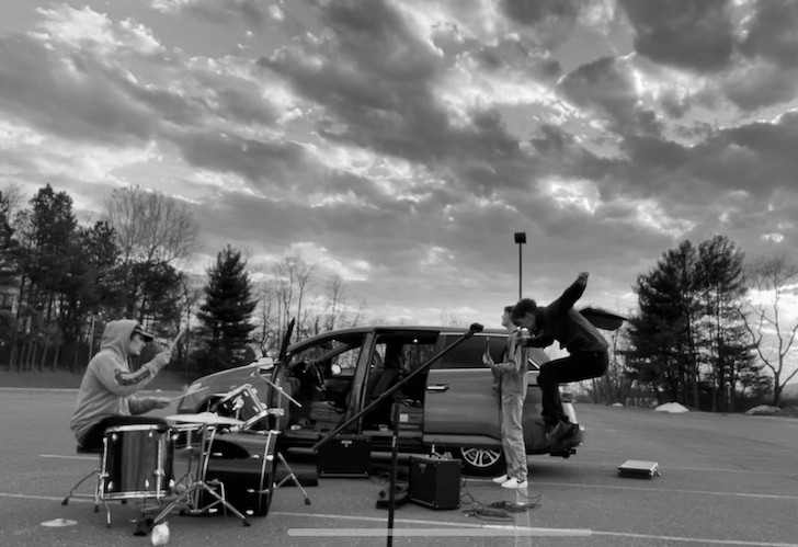 Three members of Maldición playing music by a car in a parking lot
