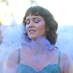 An album cover with the words 'Who Shot John' in all caps across the top and 'the frame' in all lowercase at the bottom. In the middle is an explosion of many different colors and a guy with a beard holding a guitar