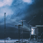 An album cover with the words 'Who Shot John' in all caps across the top and 'the frame' in all lowercase at the bottom. In the middle is an explosion of many different colors and a guy with a beard holding a guitar