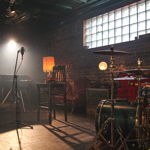 An album cover with the words 'Who Shot John' in all caps across the top and 'the frame' in all lowercase at the bottom. In the middle is an explosion of many different colors and a guy with a beard holding a guitar