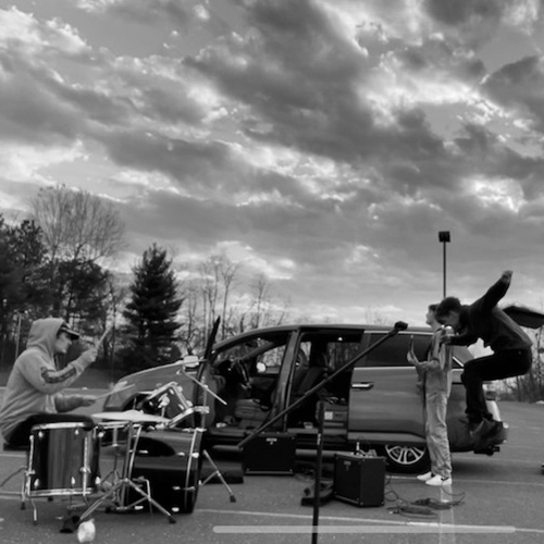 An album cover with the words 'Who Shot John' in all caps across the top and 'the frame' in all lowercase at the bottom. In the middle is an explosion of many different colors and a guy with a beard holding a guitar